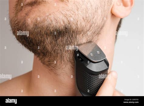Man shaving beard and neck with an electric razor. Morning routine. Trimming beard with a ...
