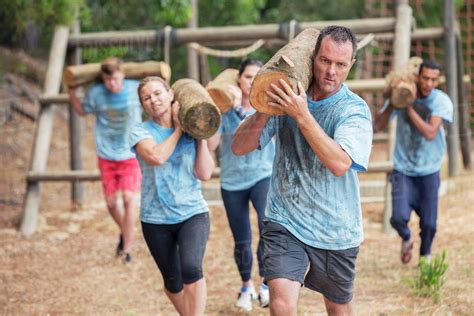 Determined people running with logs on boot camp obstacle course ...
