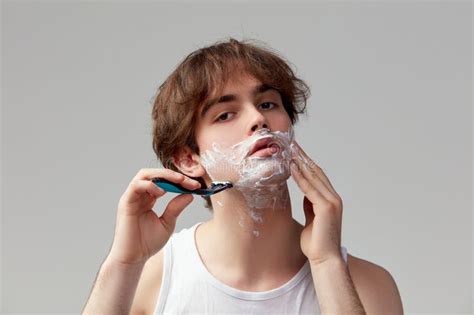 Portrait of Young Man Shaving Face with Razor and Cream, Posing Against ...