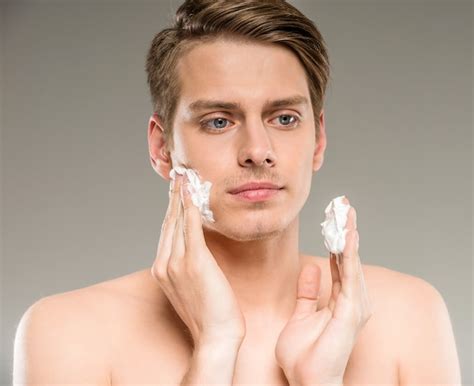 Premium Photo | Young man is applying shaving cream to his face.