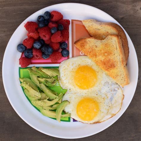 a white plate topped with eggs, toast and fruit on top of a wooden table