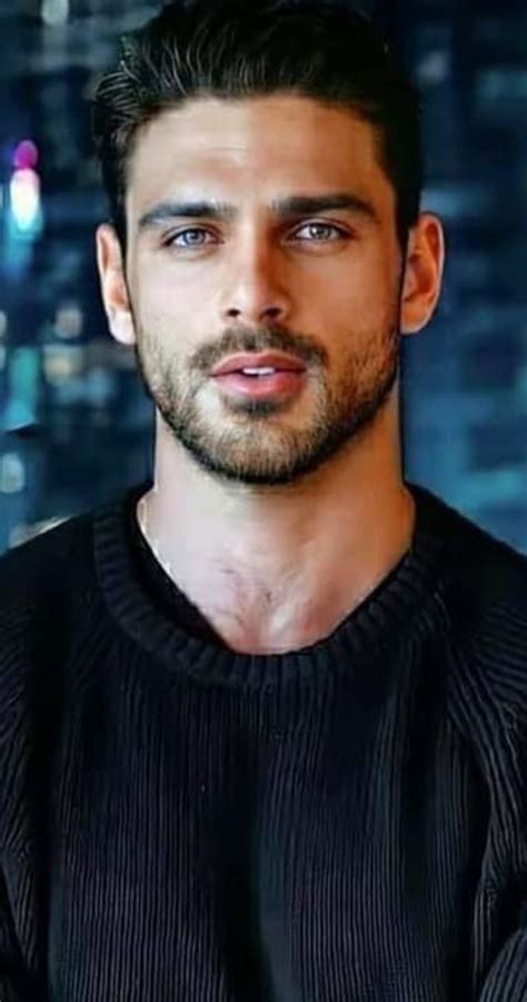 a man with a beard and black shirt in front of a cityscape at night
