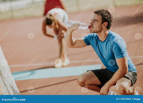 Sporty Man Drinking Water while Young Woman Doing Exercise in Th Stock ...