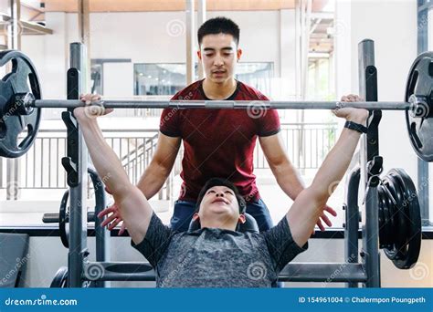 Young Asian Man Lifting Heavy Weight Working on His Upper Body Workout with His Male Trainer at ...
