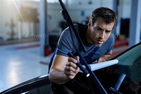 Car mechanic using flashlight while working at auto repair shop. Stock Photo by drazenphoto