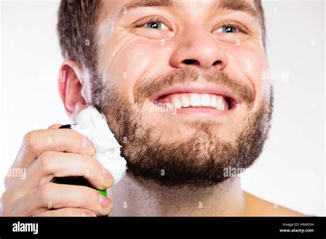 Health beauty and skin care concept. Closeup young bearded man with foam on face preparing to ...